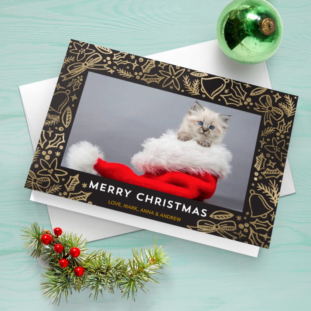 greeting card featuring cat in a santa hat, surrounded with bauble and twig