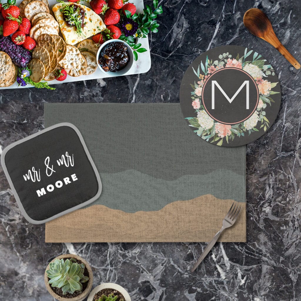 Black potholder, black stone trivet, and dark colored fabric placemat on a black marble countertop