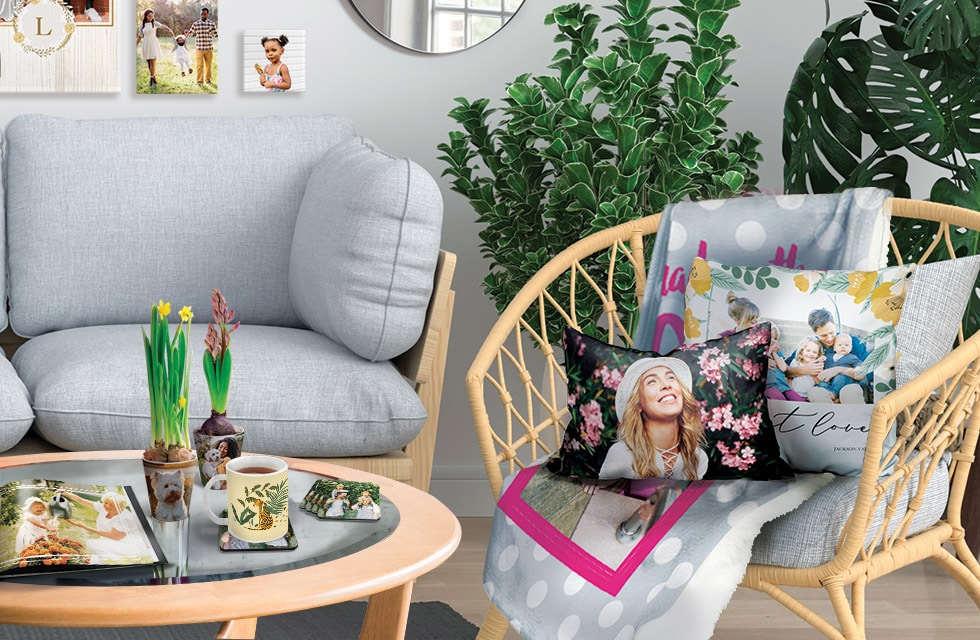 living room decor with cushions, blanket on chair, canvas on wall, photo book, plant pot, coasters and mug on table.