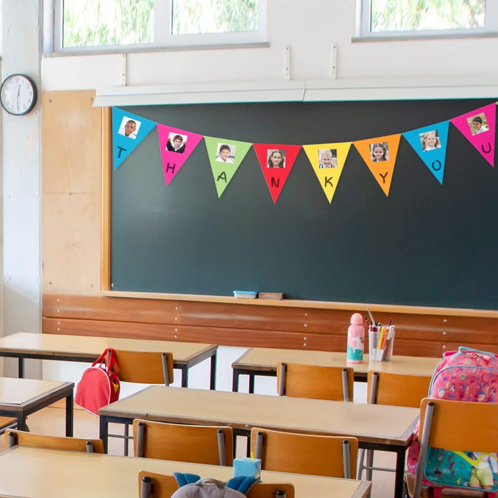 A paper bunting garland strung up over the classroom blackboard, featuring photos of each pupil in the class as a teacher thank you decoration