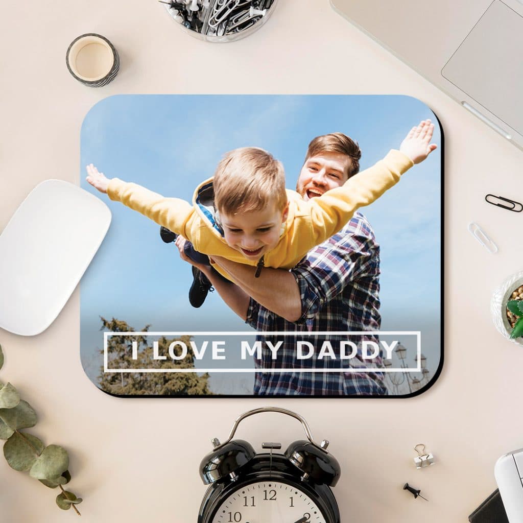 I love my daddy mousemat design with father and son picure sat on table next to alarm clock and laptop
