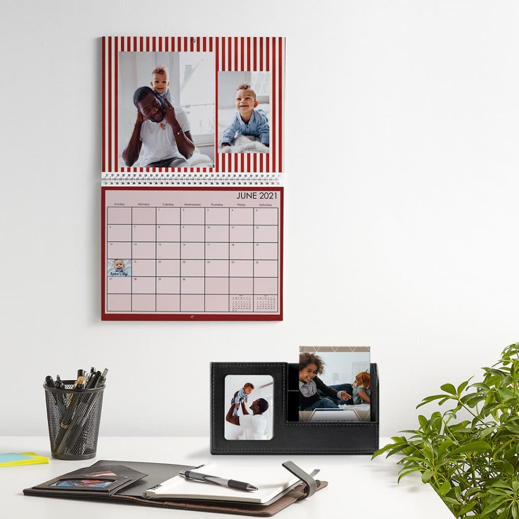 Image of a custom calendar hanging on the wall over a desk. A leatherette desk set, notebook, and more sits on the desktop.