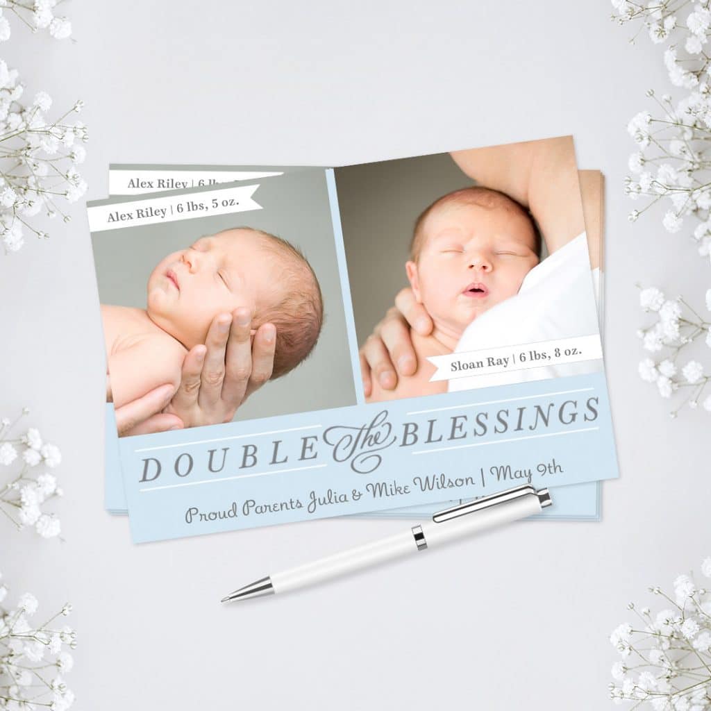 A twin baby announcement card displayed amongst flowers, alongside a white pen