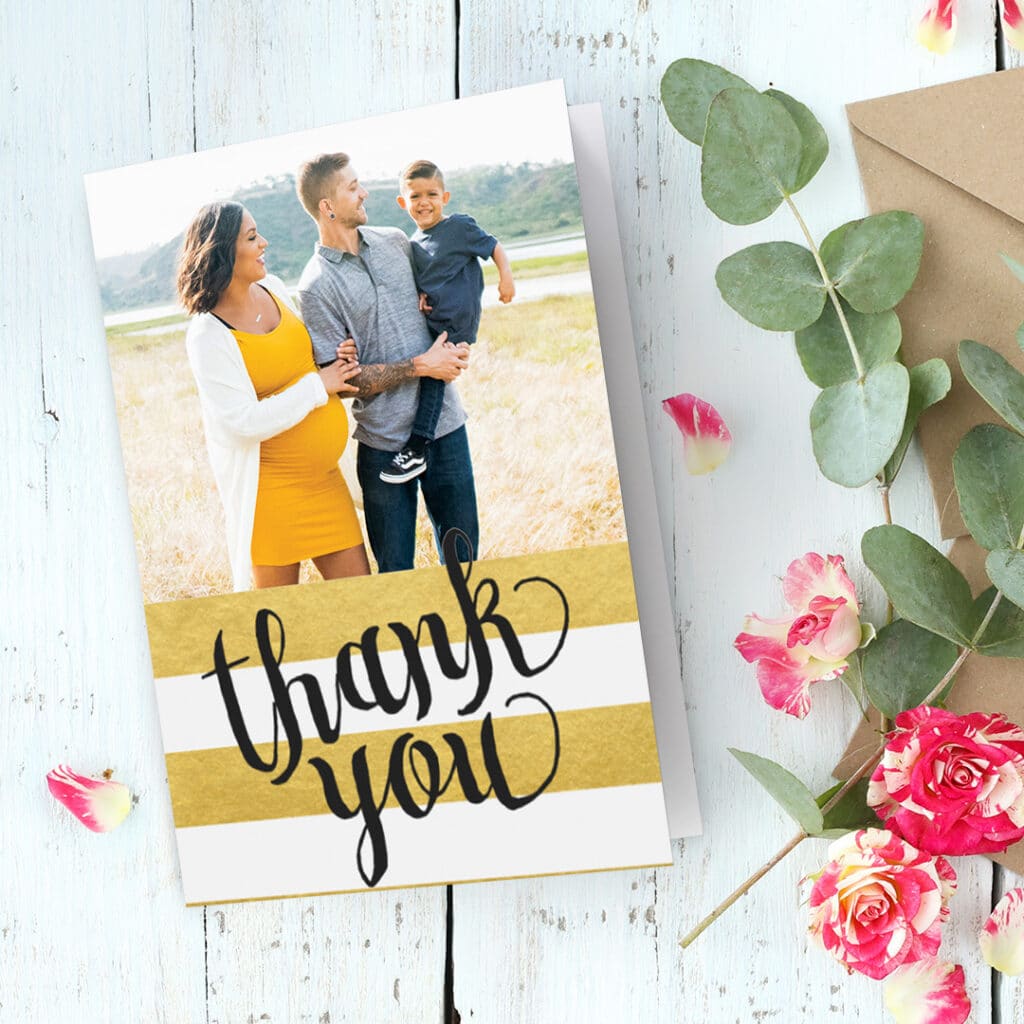 A thank you card with a family image presented on a desk with lovely colourful pink flowers
