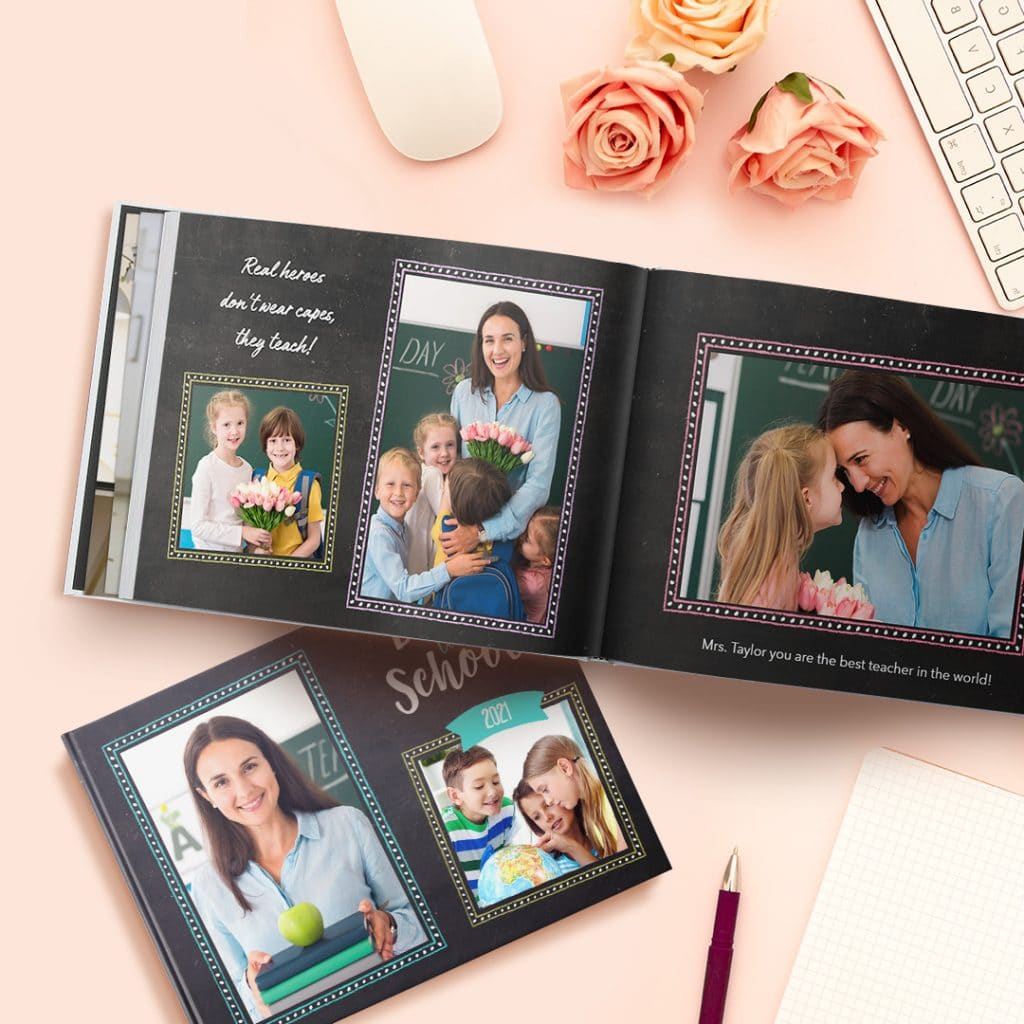 An open and a closed photo book with images of smiling children and their teacher presented on a pink surface with roses